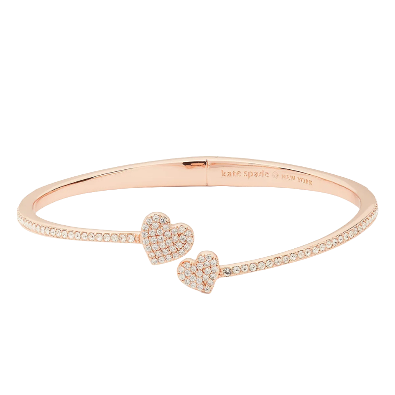 A rose gold-tone hinge cuff bracelet features two sparkling heart motifs and a row of small crystals. It is embossed with the \“kate spade new york\“ logo on the inside.