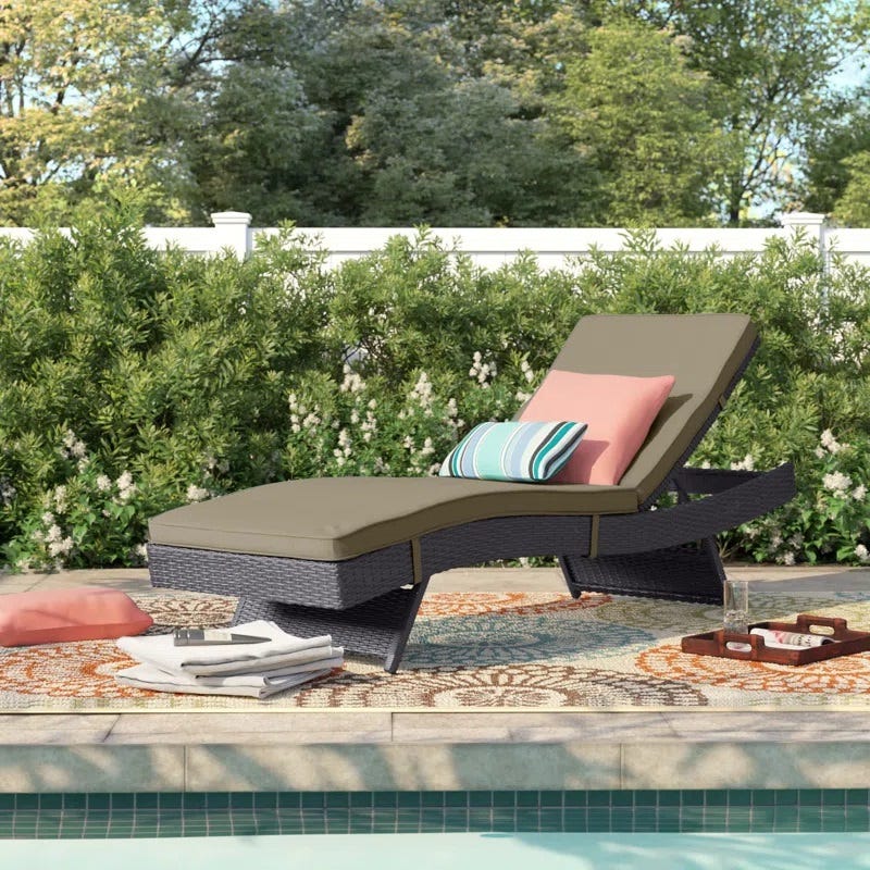 A brown wicker sun lounger with a taupe cushion, accompanied by a striped pillow and additional poolside accessories.