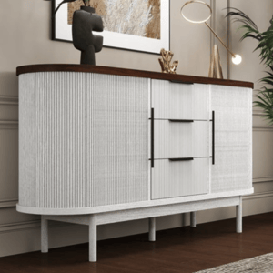 A modern sideboard features a white textured design with a dark wood top, decorated with a vase, abstract sculpture, and a small table lamp. It is set against a beige wall with a large framed artwork and accompanied by a tall potted plant.