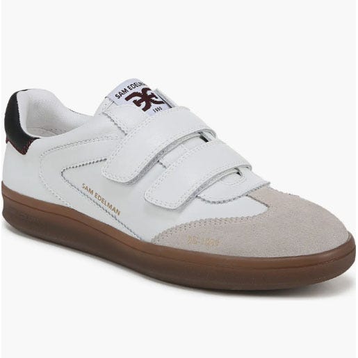 A white sneaker with two velcro straps, featuring a suede toe, a brown sole, and \“SAM EDELMAN\“ branding on the side.