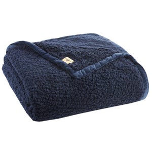 A folded dark blue sherpa throw blanket with a satin trim, featuring a small fabric tag.