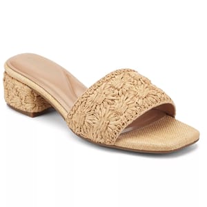 A beige, woven heeled sandal with an open toe, featuring a low block heel and intricate floral pattern on the strap.
