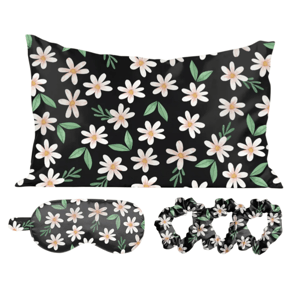 A black pillowcase, eye mask, and set of scrunchies featuring a white daisy and green leaf pattern.