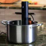 A stainless steel pot with handles, containing an immersion circulator or sous-vide cooker, is placed on a kitchen countertop.