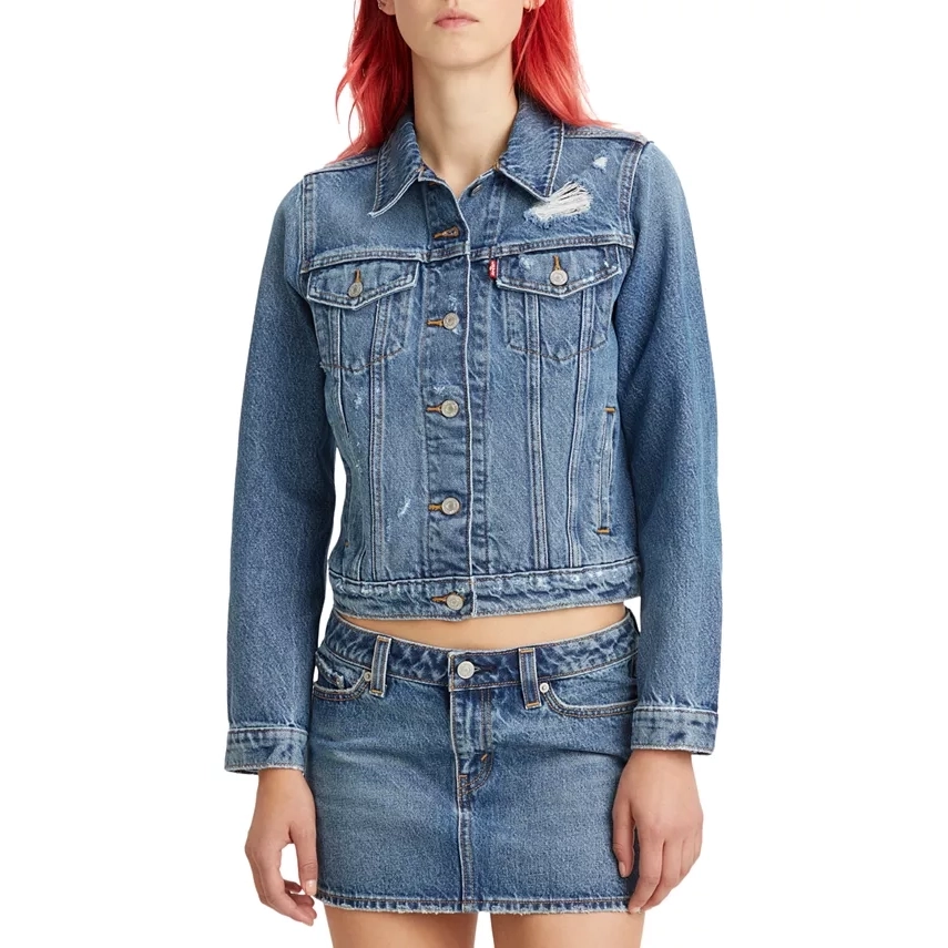 A person wearing a denim jacket and skirt set with a distressed design.