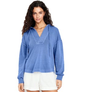 A woman is wearing a blue hoodie-style pullover with a V-neck and drawstring, paired with white shorts.