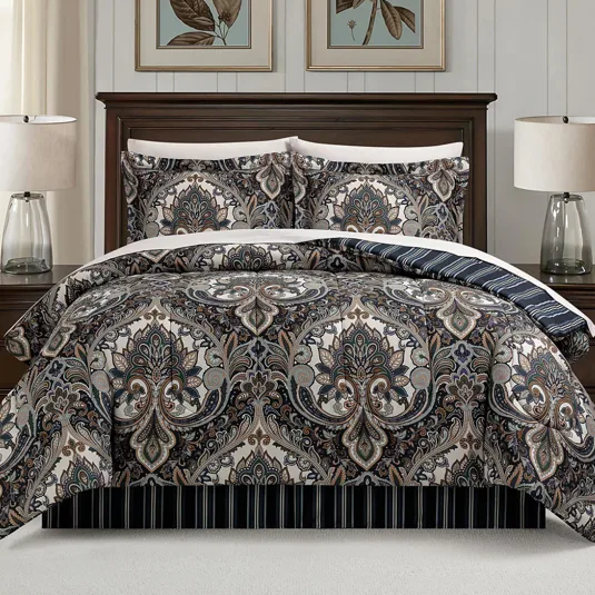 A bed set featuring a detailed paisley pattern with matching pillow shams, set against a dark wooden bed frame. Two table lamps with clear glass bases are on the nightstands beside the bed.