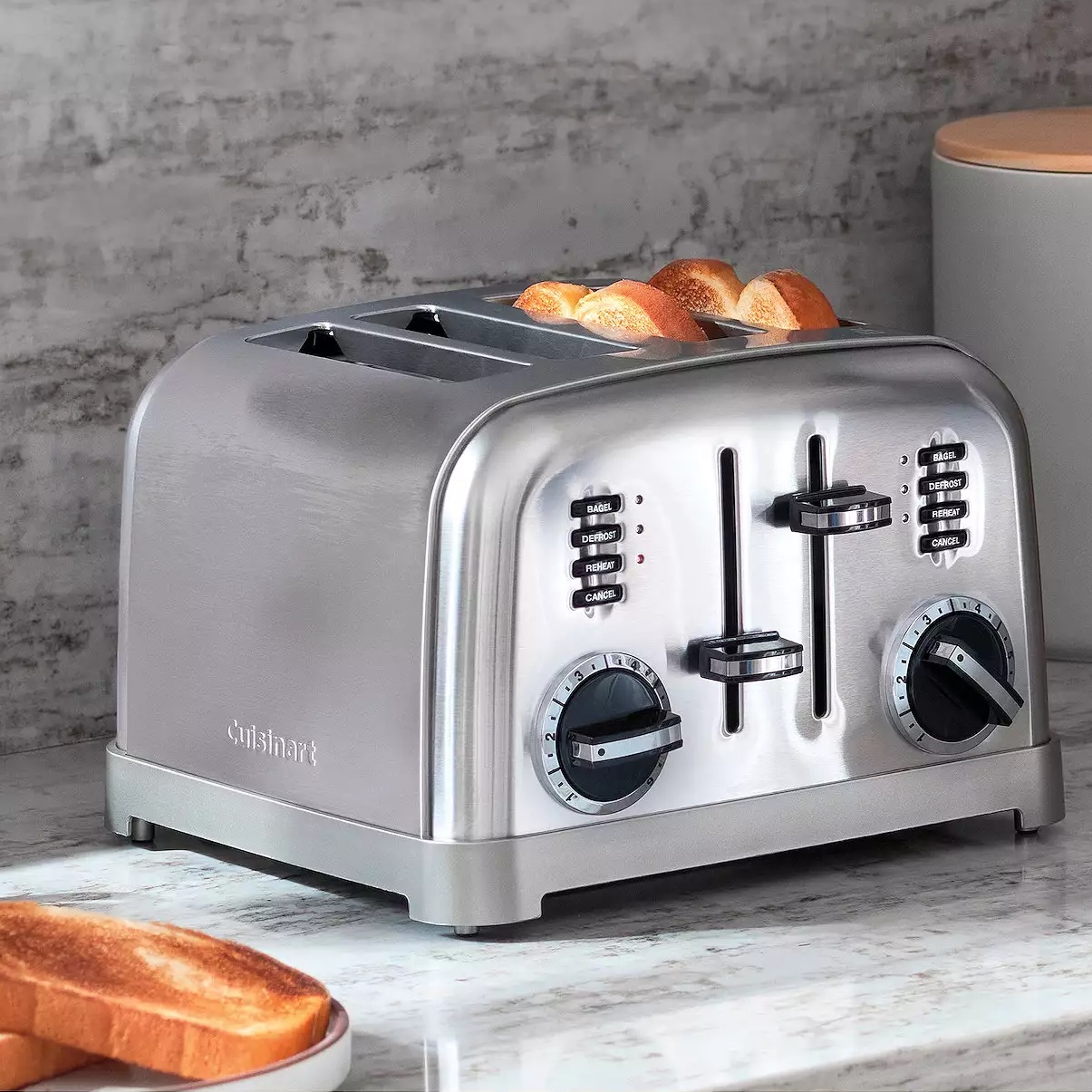 A stainless steel four-slice toaster with dual control panels and toast popping up.