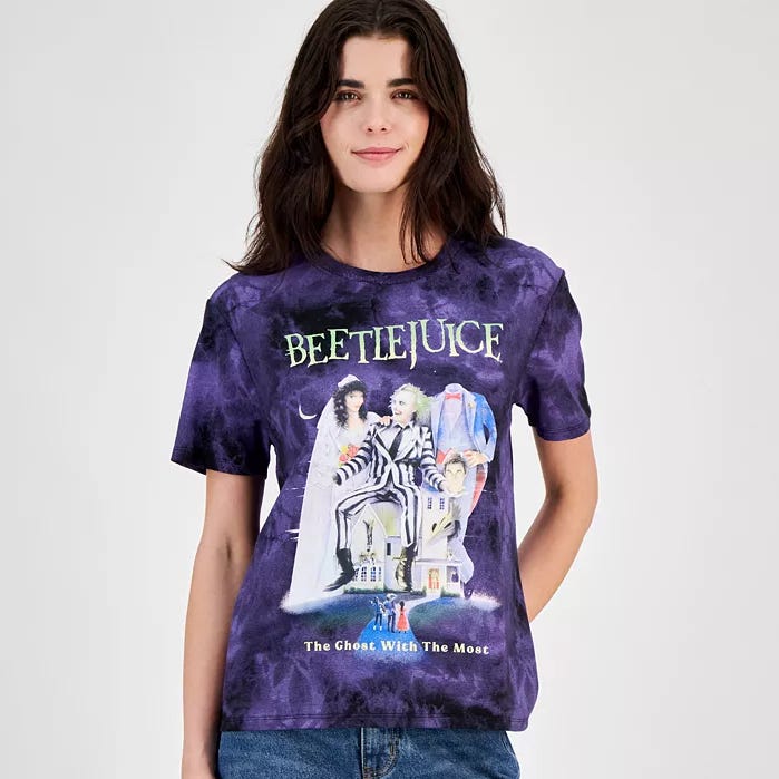 A person is wearing a purple tie-dye T-shirt with a \“Beetlejuice\“ movie theme and the tagline \“The Ghost With The Most.\“