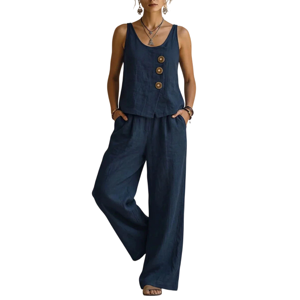 A person stands against a wall wearing a sleeveless navy top with three large buttons and matching wide-leg pants, accessorized with necklaces and bracelets.