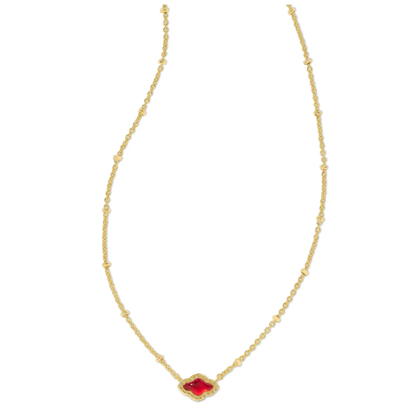 A gold chain necklace features a red clover-shaped mini pendant with a mother-of-pearl inlay, accented by smaller, evenly spaced embellishments along the chain.