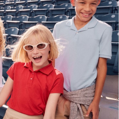 Two children are wearing short-sleeved polo shirts, one in red and the other in pale blue, both with collars and a few buttons at the neck.