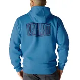 Blue Carhartt hoodie with a large logo on the back, worn by a person facing away, paired with dark pants.