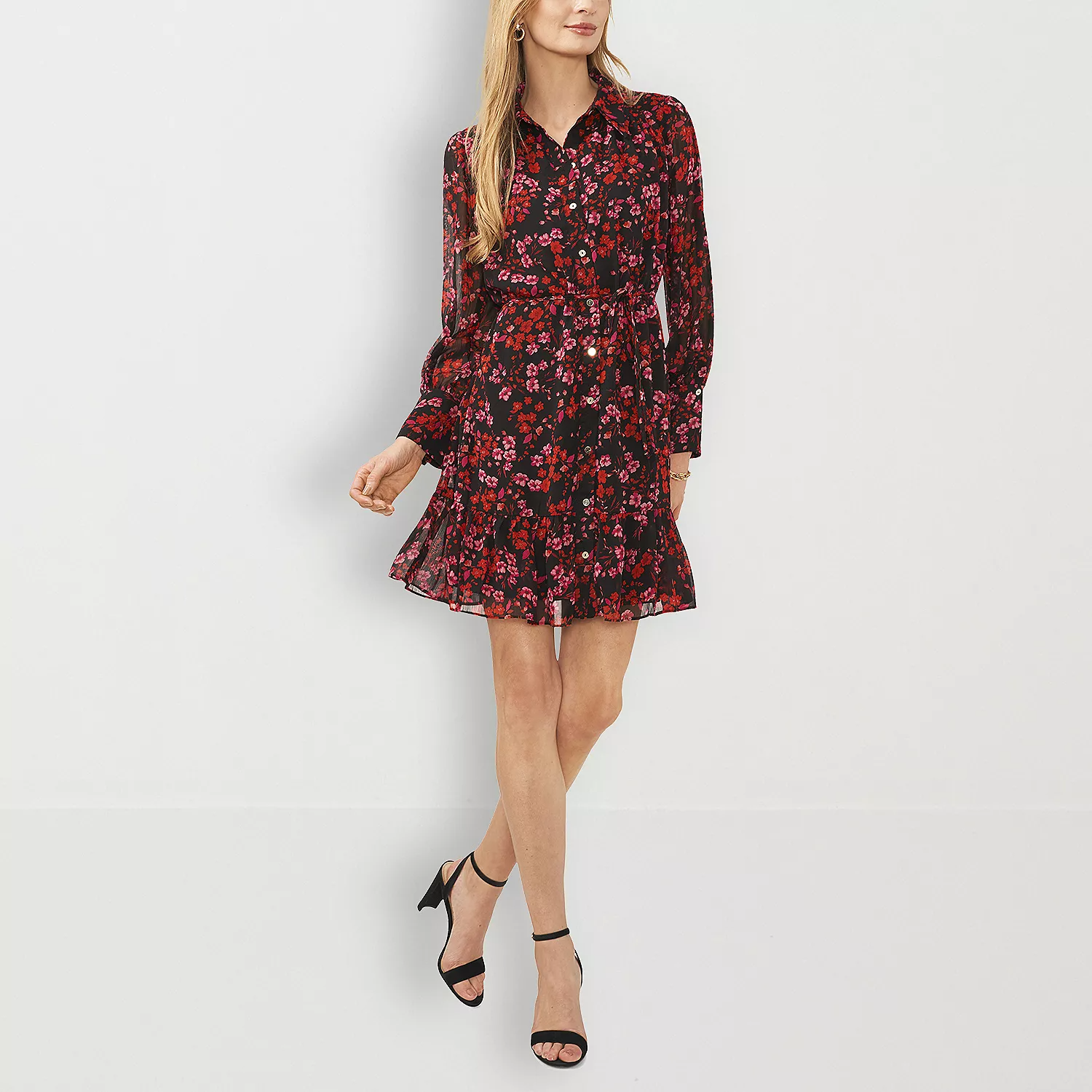 A woman is wearing a black floral print dress with long sleeves and a belted waist, accompanied by black ankle-strap high heels.
