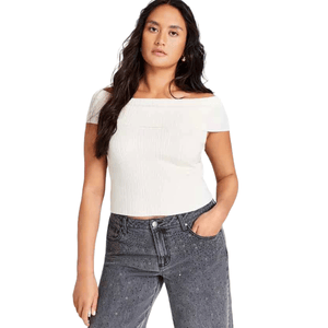 A woman is wearing an off-the-shoulder white top with short sleeves and a textured pattern, paired with high-waisted dark wash jeans featuring subtle embellishments.