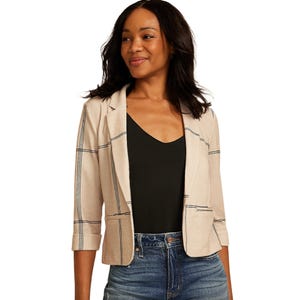 A woman wearing a beige plaid blazer with three-quarter sleeves over a black top and blue jeans.