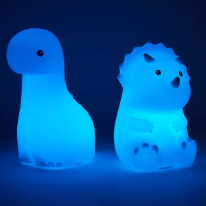 Two dinosaur-shaped night lights emit a blue glow; one resembles a brachiosaurus, and the other resembles a triceratops.
