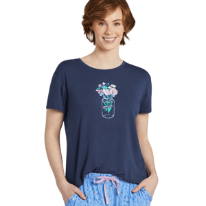 Woman wearing a navy blue T-shirt with a floral jar design and light blue pajama pants featuring a floral pattern and pink drawstring.