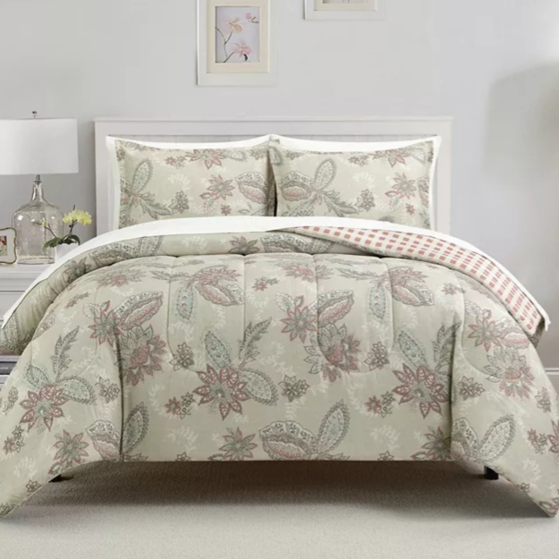 A white bed with a floral-patterned comforter set, including two matching pillow shams, is flanked by two white nightstands with lamps and decorative items. The wall features two framed prints and small windows, creating a cozy, coordinated bedroom look.