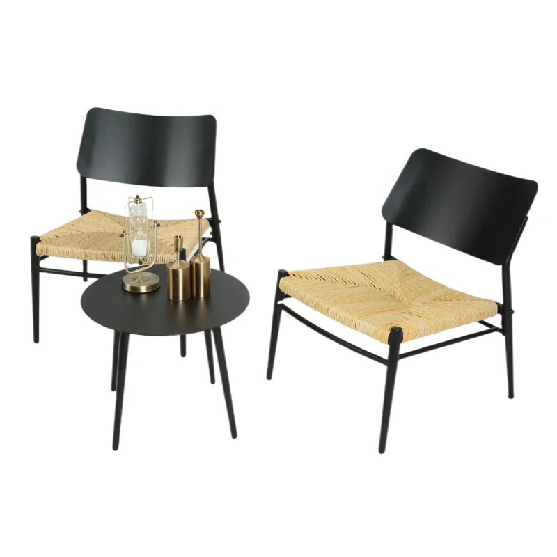 Two black chairs with woven rattan seats and a matching round black table featuring a chemex coffee maker and brass-colored accessories.