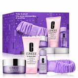 Clinique's \“Take it all off\“ skincare set includes a cleansing balm, rinse-off foaming cleanser, makeup remover for lids, lashes, and lips, and a purple headband in a purple-themed box.
