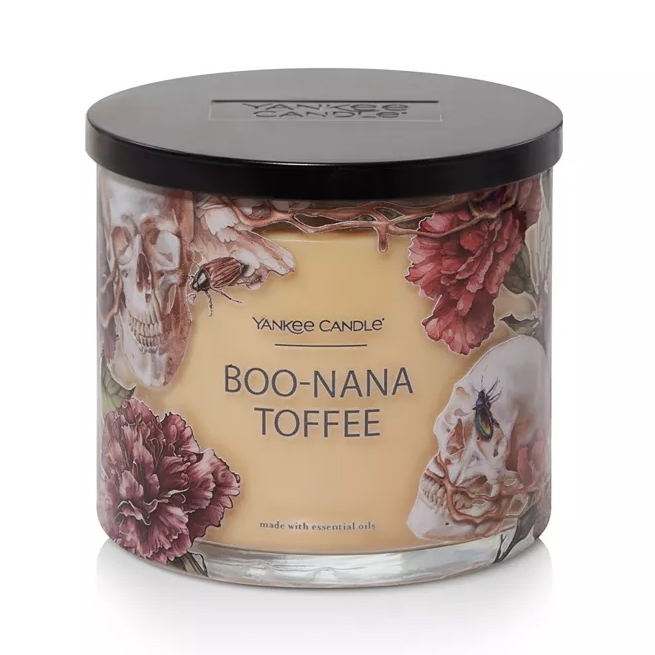 Yankee Candle \“Boo-Nana Toffee\“ features a spooky design with skulls, flowers, and insects, and is made with essential oils.