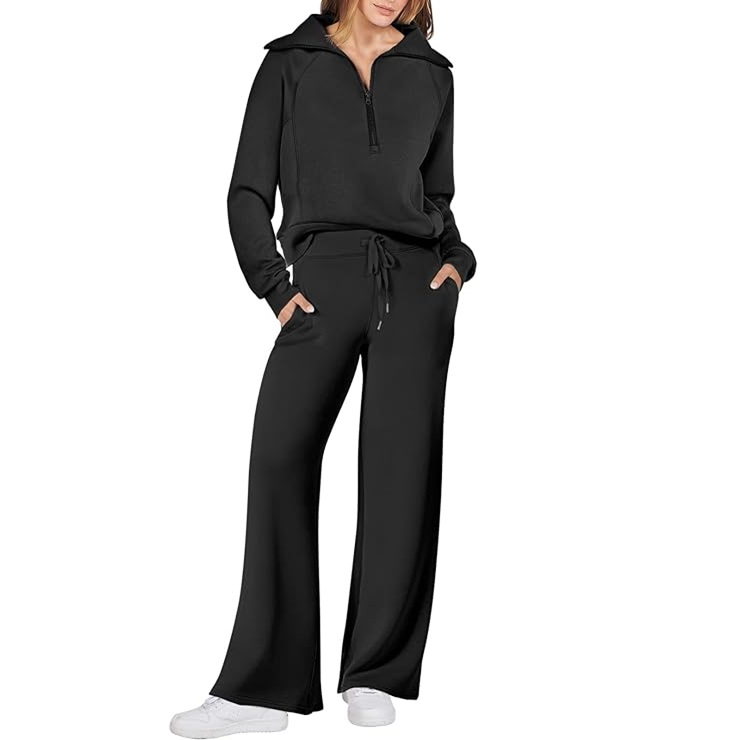 A woman is wearing a black hoodie with a zipper and drawstring, paired with black wide-leg pants and white sneakers.