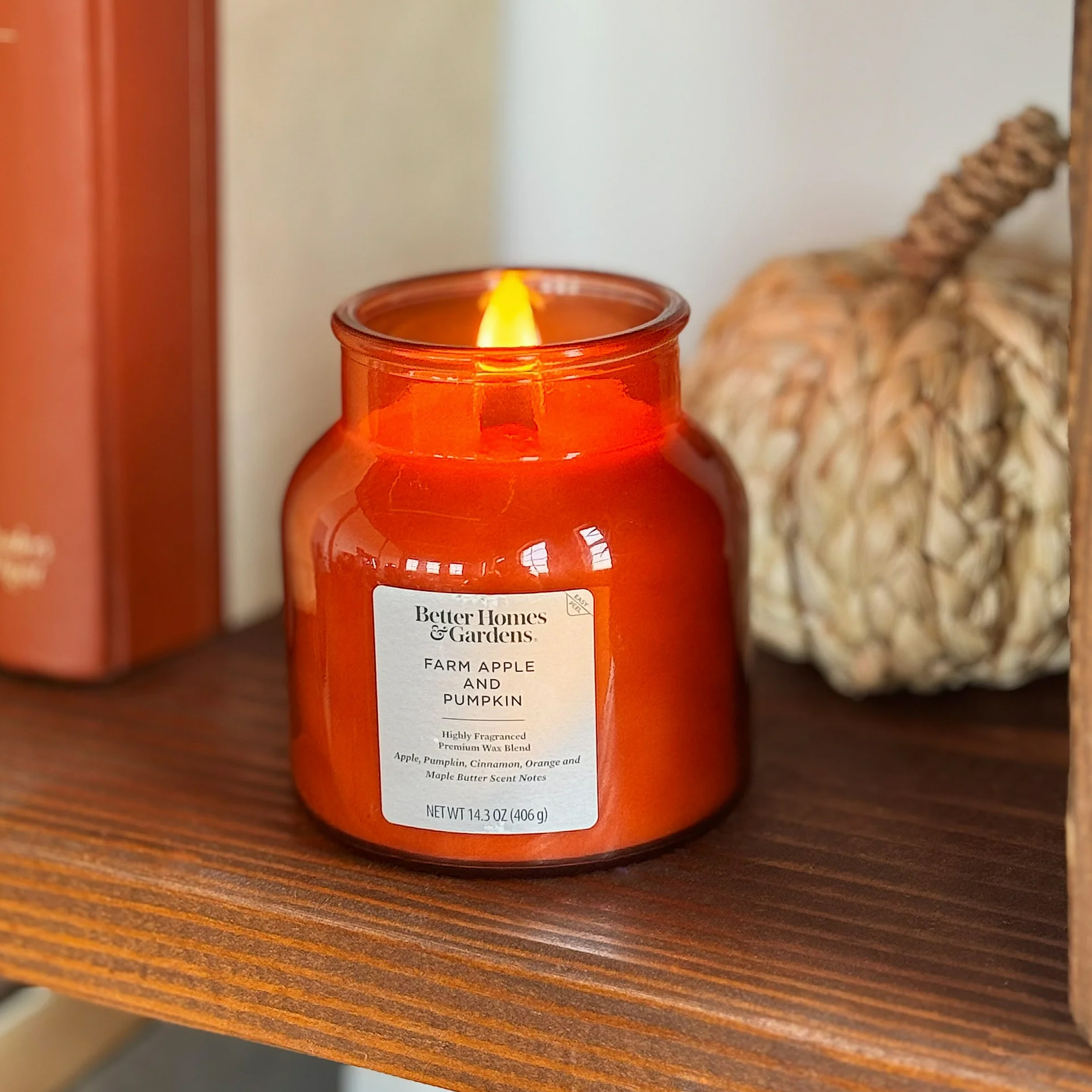 A lit orange candle from Better Homes & Gardens with a Farm Apple Pumpkin scent.