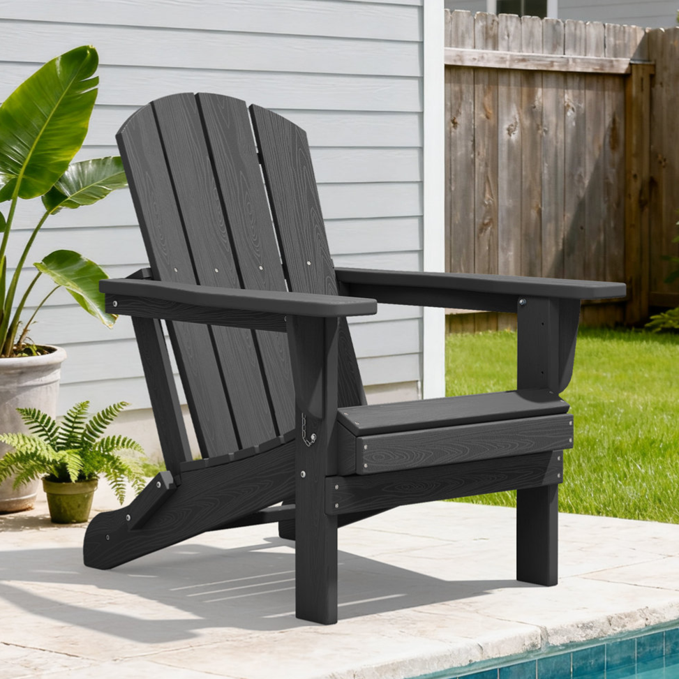A black Adirondack chair is positioned by a poolside, with a surrounding setting featuring green grass, potted plants, and a wooden fence.