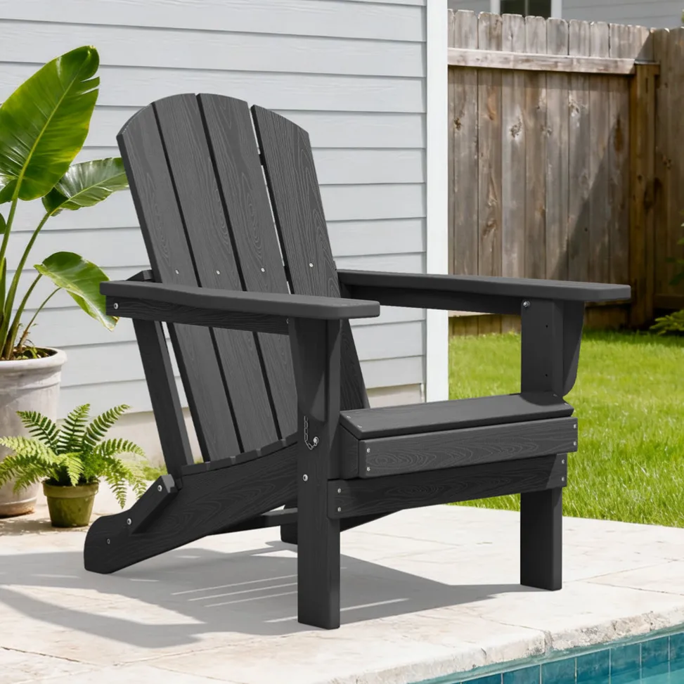 A black Adirondack chair is positioned by a poolside, with a surrounding setting featuring green grass, potted plants, and a wooden fence.