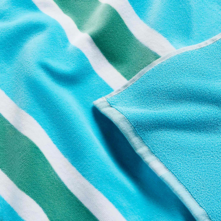 A teal and white striped beach towel with a close-up view showing the texture and stitching details.