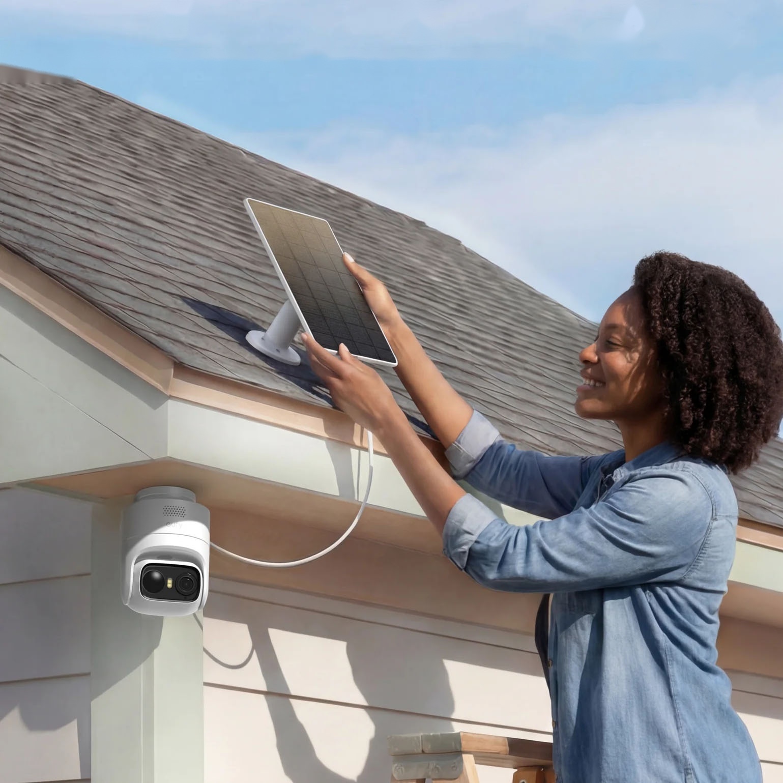 A person is installing a solar panel connected to a security camera mounted on the side of a house.