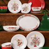 Festive dinnerware collection with Christmas tree and ribbon motifs, featuring plates, bowls, and an oval platter. Includes green and red solid color pieces, and a tree-shaped tray. Perfect for holiday settings.