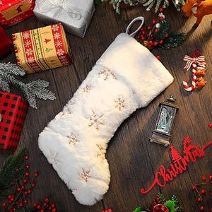 A white plush Christmas stocking is shown with embroidered snowflakes, accompanied by winter-themed decorations and gifts.