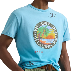 A blue T-shirt featuring a vintage-style graphic with \“1967 Ralph Lauren Pacific,\“ palm trees, a sunset, and the text \“R.S.C 91.\“