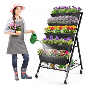 A woman in gardening attire is watering flowers on a multi-tiered plant stand.