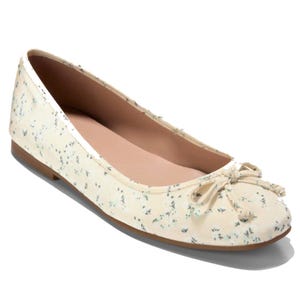 A cream-colored ballet flat with a subtle floral print and a small bow on the toe.