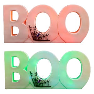Two decorative signs spell \“BOO\“ with a spiderweb and spider detail, one lit in red-orange and the other in green-blue hues.