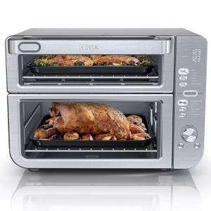Ninja DoubleStack XL Oven is a countertop appliance with two cooking compartments, allowing for simultaneous baking and roasting. It features digital controls and a stainless steel finish, shown roasting a chicken and vegetables on the bottom and baking on the top.