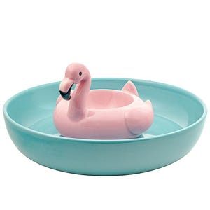 A ceramic chip and dip bowl featuring a pink flamingo in the center, resembling a pool floatie. The bowl is turquoise, with the flamingo serving as the dip holder.