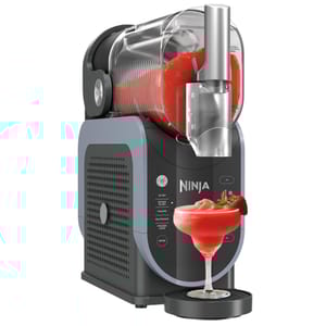 Refurbished Ninja SLUSHi is a slushie maker with a sleek black and gray design, featuring a clear cylindrical container for mixing. It dispenses red slush into a glass, highlighting its beverage-making capability.
