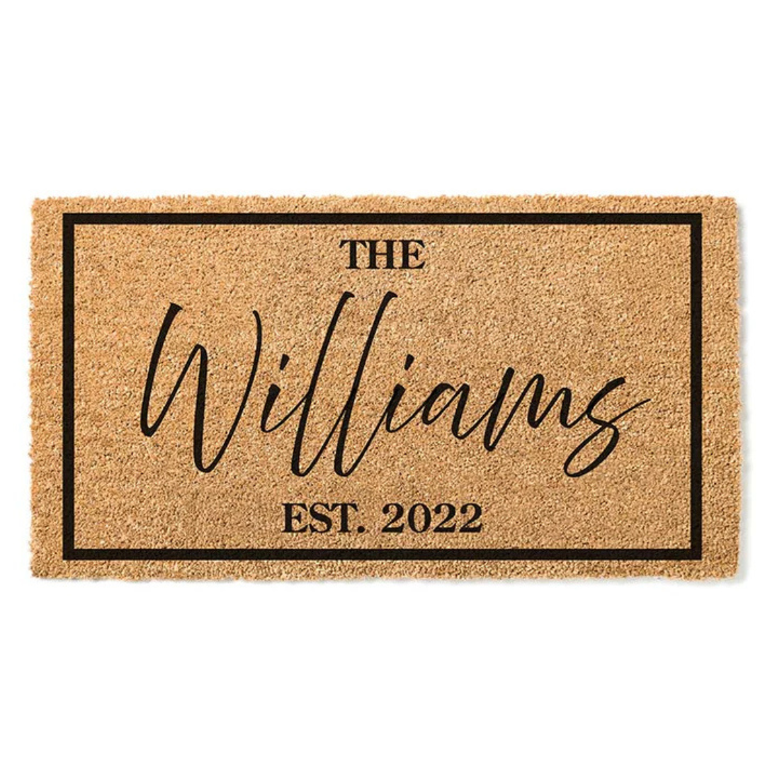 A coir doormat with a black border features the text \“The Williams\“ in a cursive script and \“Est. 2022\“ in a bold font.