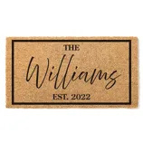 A coir doormat with a black border features the text \“The Williams\“ in a cursive script and \“Est. 2022\“ in a bold font.