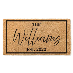 A coir doormat with a black border features the text \“The Williams\“ in a cursive script and \“Est. 2022\“ in a bold font.