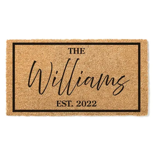 A coir doormat with a black border features the text \“The Williams\“ in a cursive script and \“Est. 2022\“ in a bold font.