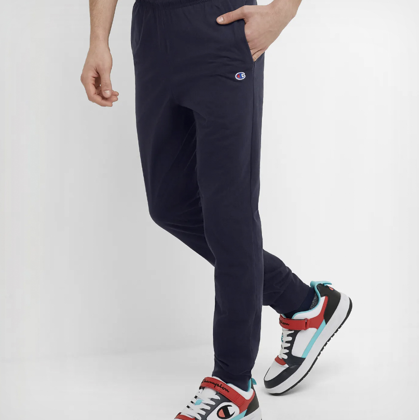 A person wearing dark blue track pants with a logo on the left thigh and multicolored sneakers.