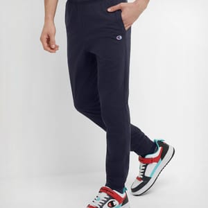 A person wearing dark blue track pants with a logo on the left thigh and multicolored sneakers.