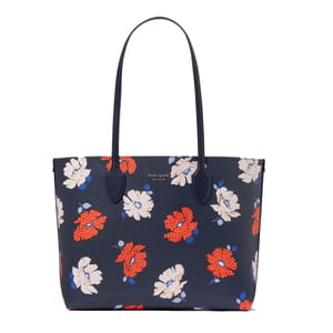 A navy tote bag with long handles featuring a floral pattern with red, white, and blue flowers. \“Kate Spade New York\“ is printed on the front.