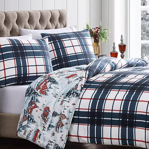 A bed with plaid bedding and a pattern of horses and skiers on the reverse side of the comforter.