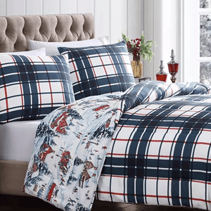 A bed with plaid bedding and a pattern of horses and skiers on the reverse side of the comforter.